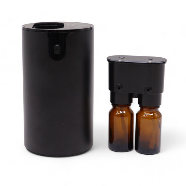 Nébuliseur cylindrique noir mat, posé à côté de sa tête amovible sur laquelle sont vissés deux flacons ambrés