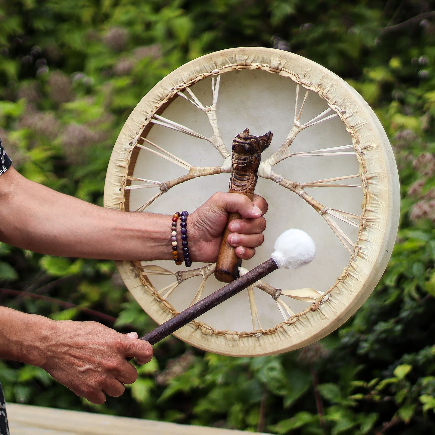 Le tambour tenu à la main par sa poignée sculptée, mailloche dans l'autre main, en extérieur