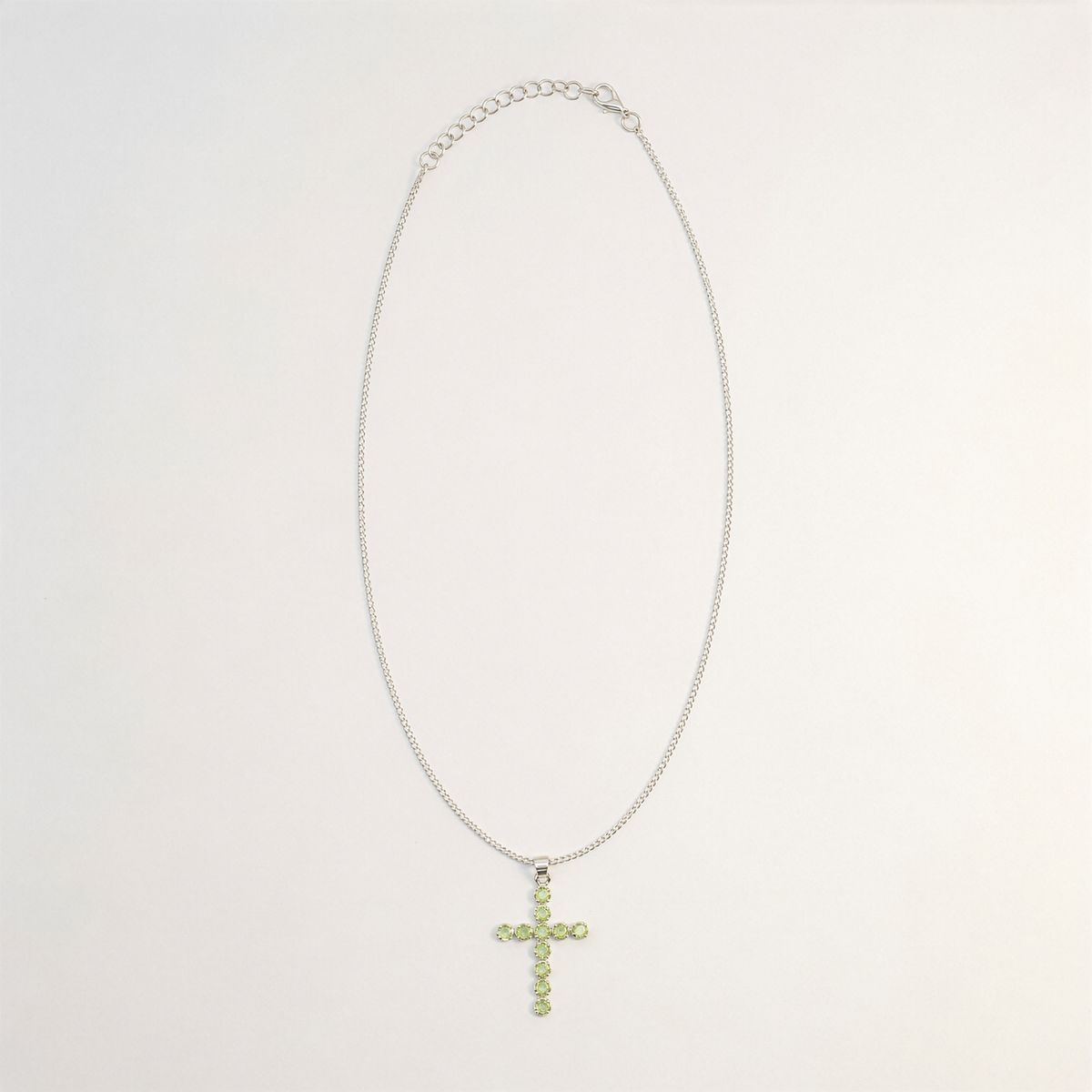 Pendentif croix en métal argenté serti de petits péridots vert clair, sur chaîne fine