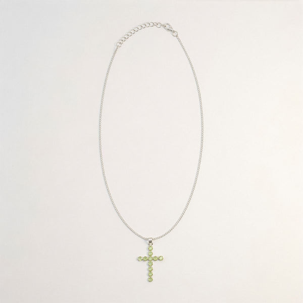 Pendentif croix en métal argenté serti de petits péridots vert clair, sur chaîne fine