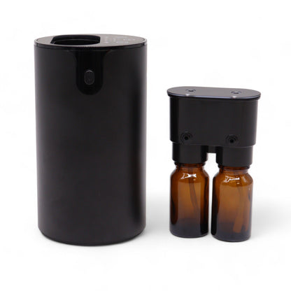 Nébuliseur cylindrique noir mat, posé à côté de sa tête amovible sur laquelle sont vissés deux flacons ambrés