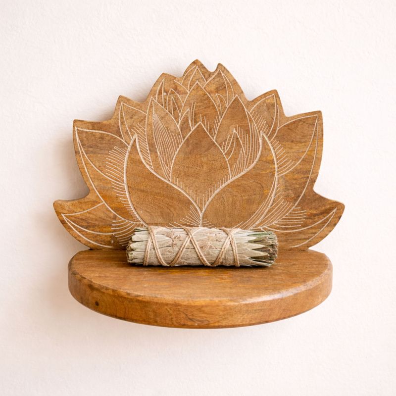 L'étagère lotus accrochée à un mur crème, avec un fagot de sauge blanche posé sur la tablette