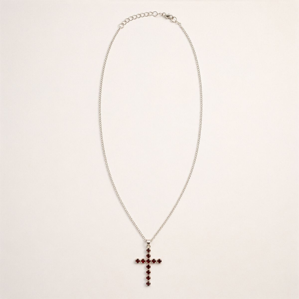 Pendentif croix en métal argenté serti de petits grenats rouge sombre, sur chaîne fine